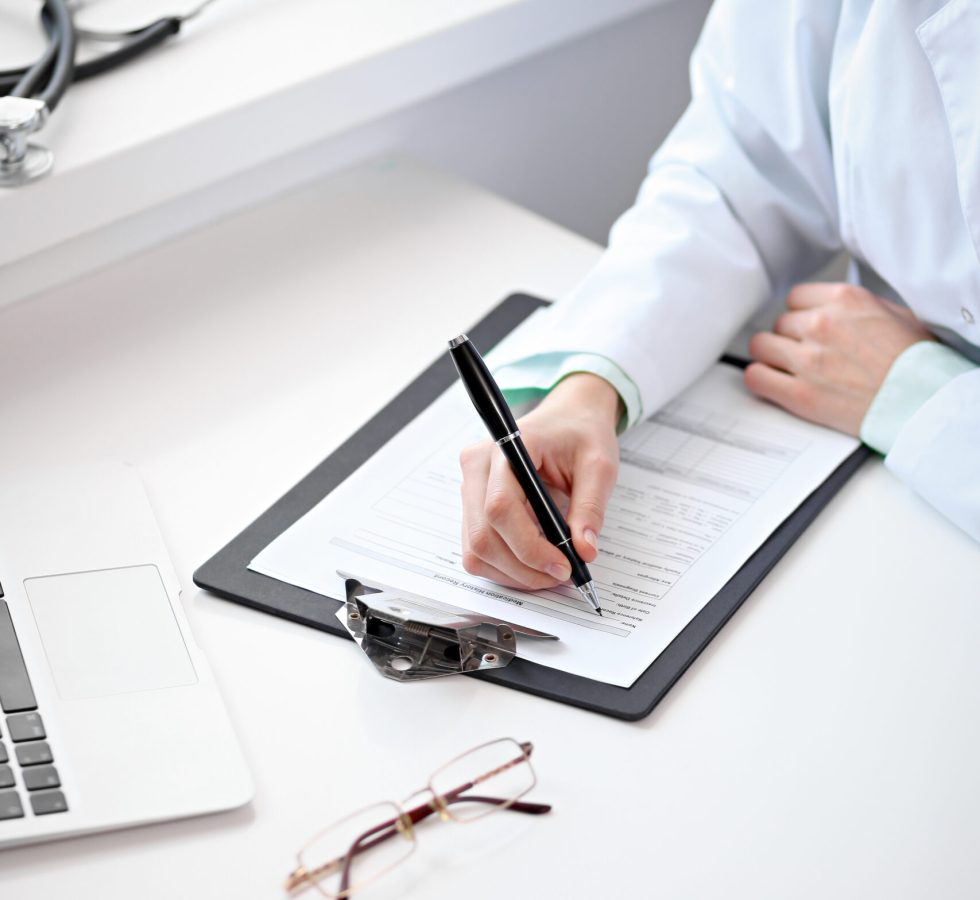 Close up of  unknown female doctor sitting  at the table near the window in hospital and typing at laptop computer